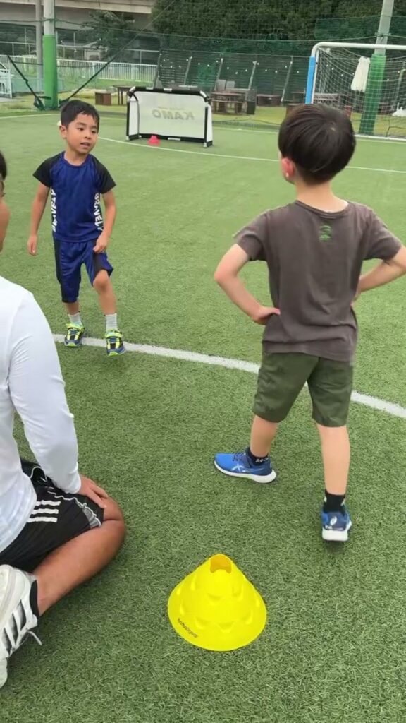 コーチが人工芝に座り、幼児クラスのお子さまと同じ目の高さで向き合っている様子